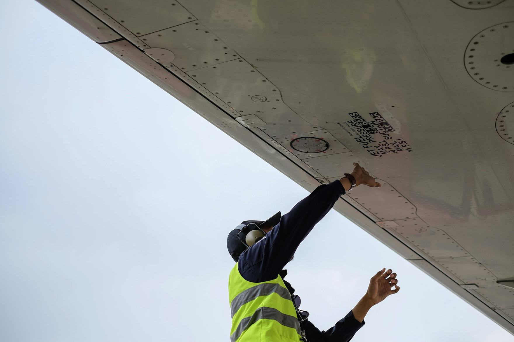 Technician in high-visibility clothing inspecting the underside of an aircraft wing